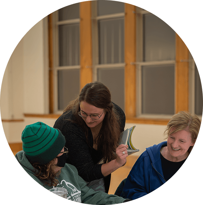 Teacher assisting two students seated at a table during a lesson.