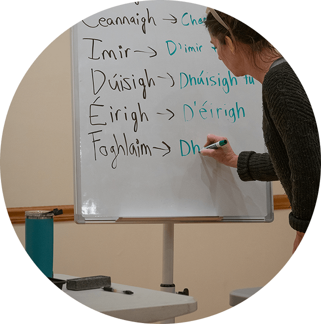 A woman writing in Gaelic on a whiteboard.