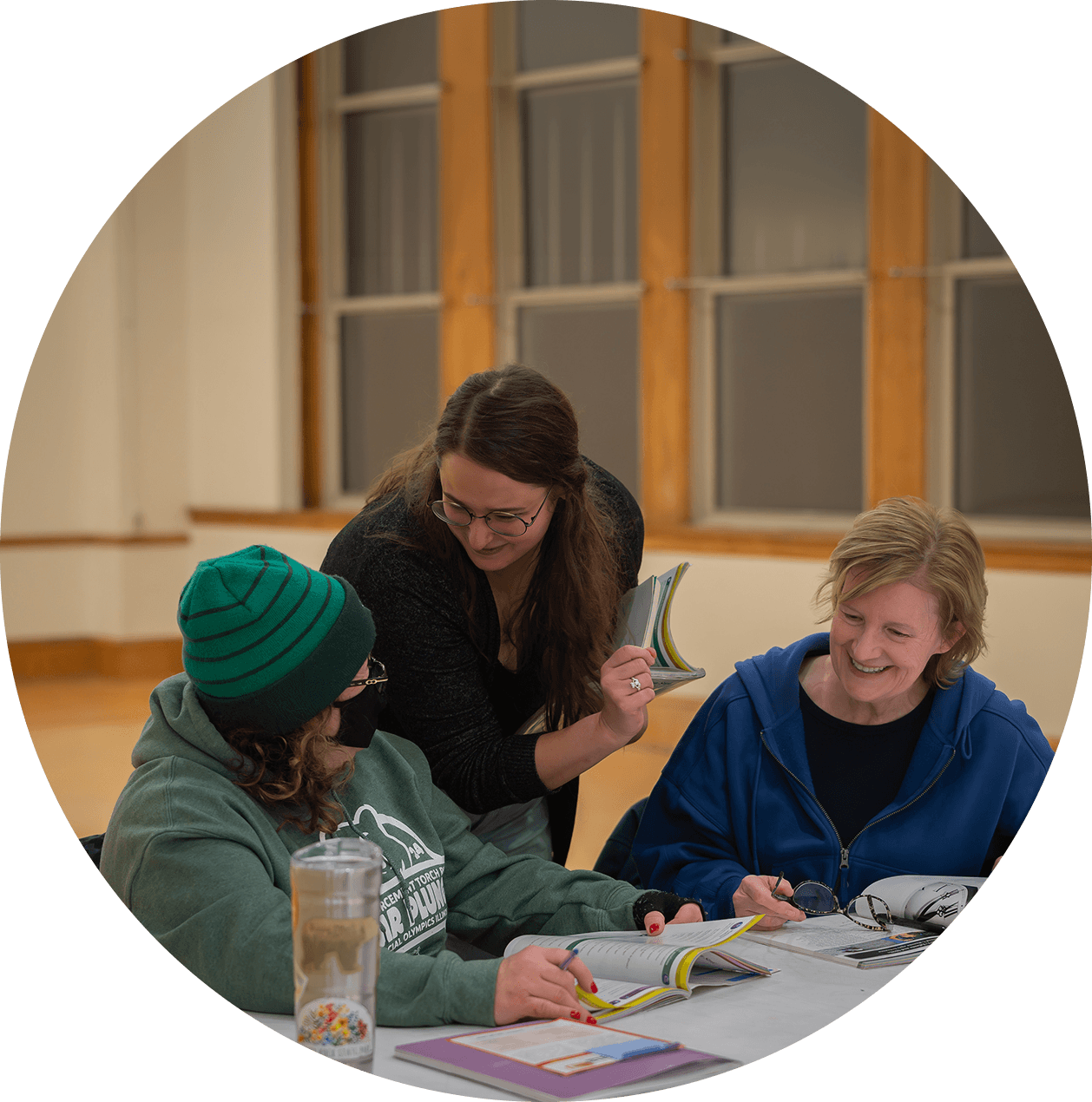 Teacher assisting two students seated at a table during a lesson.
