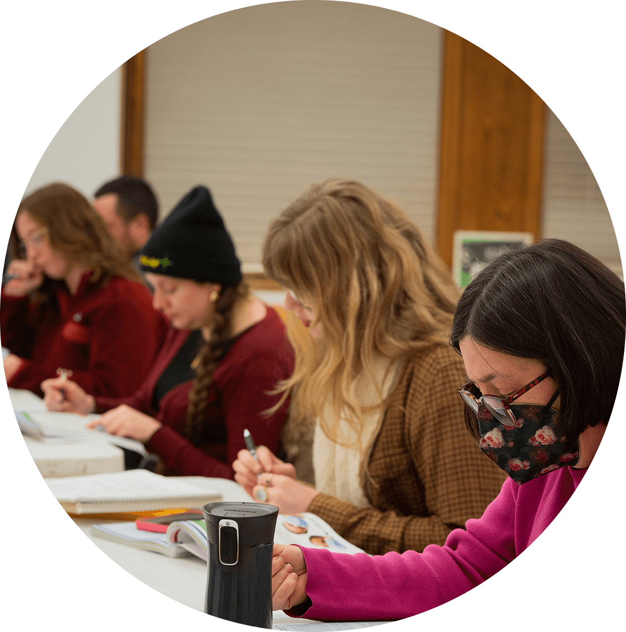 Students along a table studying from workbooks.