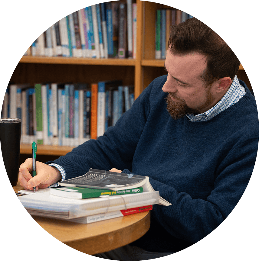 Student taking notes at a table with books on the table.